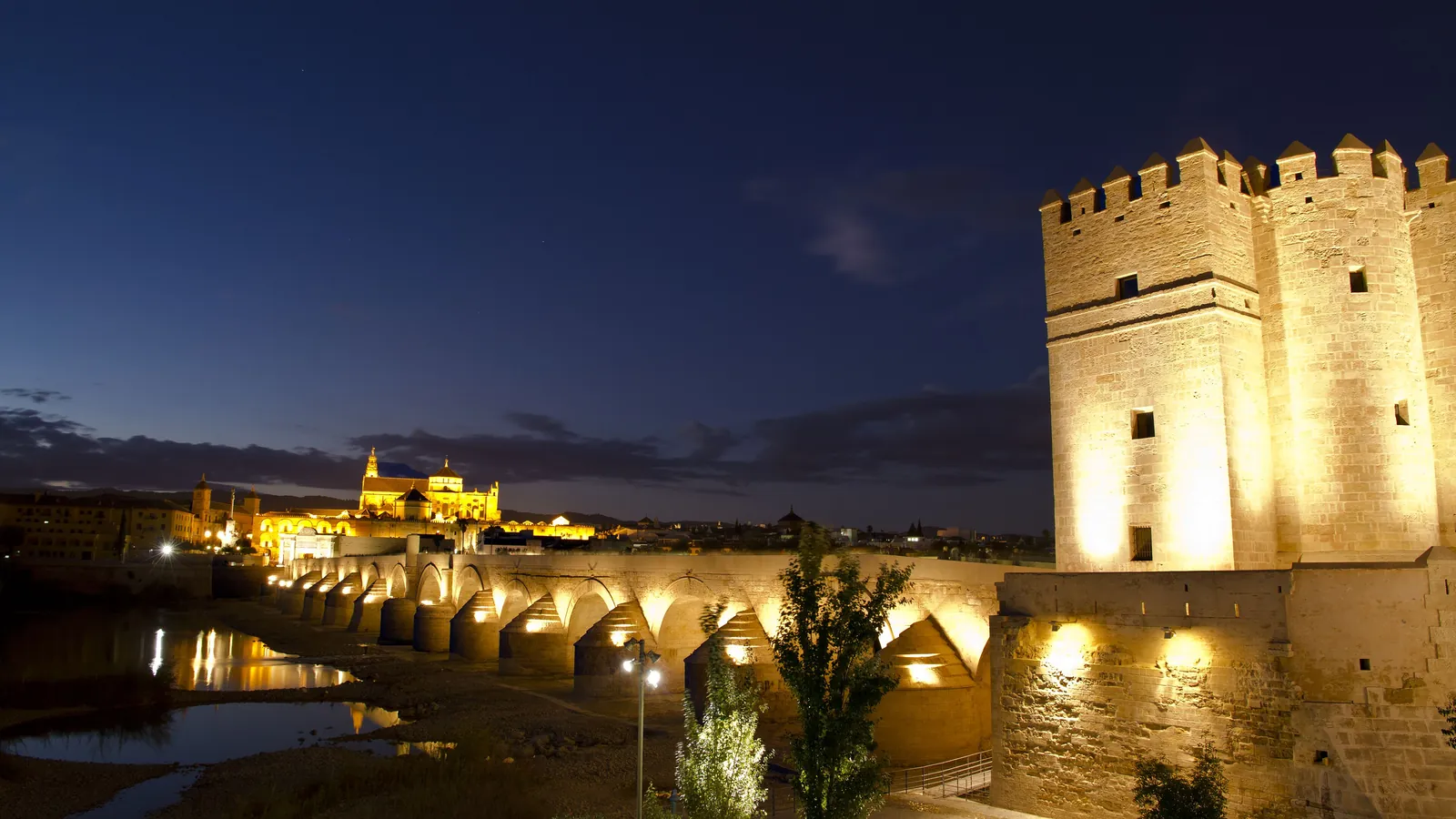 Věž Calahorra, římský most přes Guadalquivir a v dálce osvětlená Mešita-katedrála pod hluboce modrou večerní oblohou