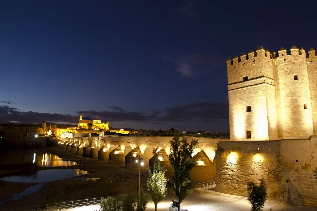 Věže Calahorra, římský most přes Guadalquivir a v dálce osvětlená Mešita-katedrála pod hlubokou modrou večerní oblohou