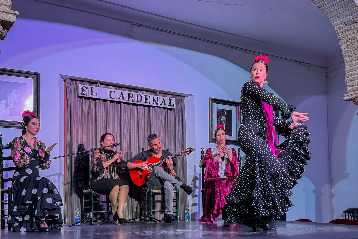 Flamenková tanečnice v černých šatech s puntíky uprostřed otáčky v Tablao El Cardenal, za ní kytarista, zpěvák a dvě sedící tanečnice